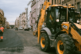 Ein geparkter Tieflöffelbagger auf einer Baustelle vor mehreren Gebäuden.