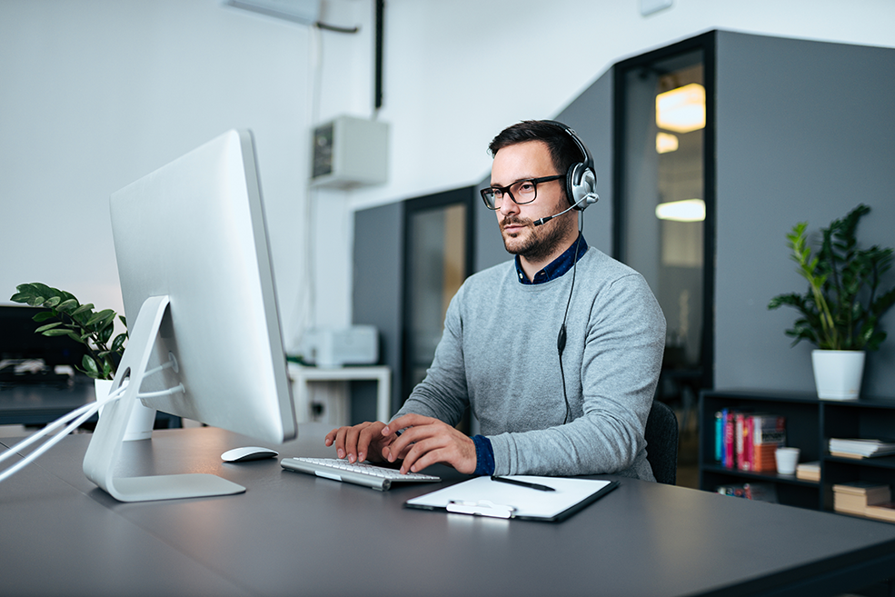 Junger IT-Experte mit Headset, der mit Infrastrukturanalysen an einem Computer arbeitet.