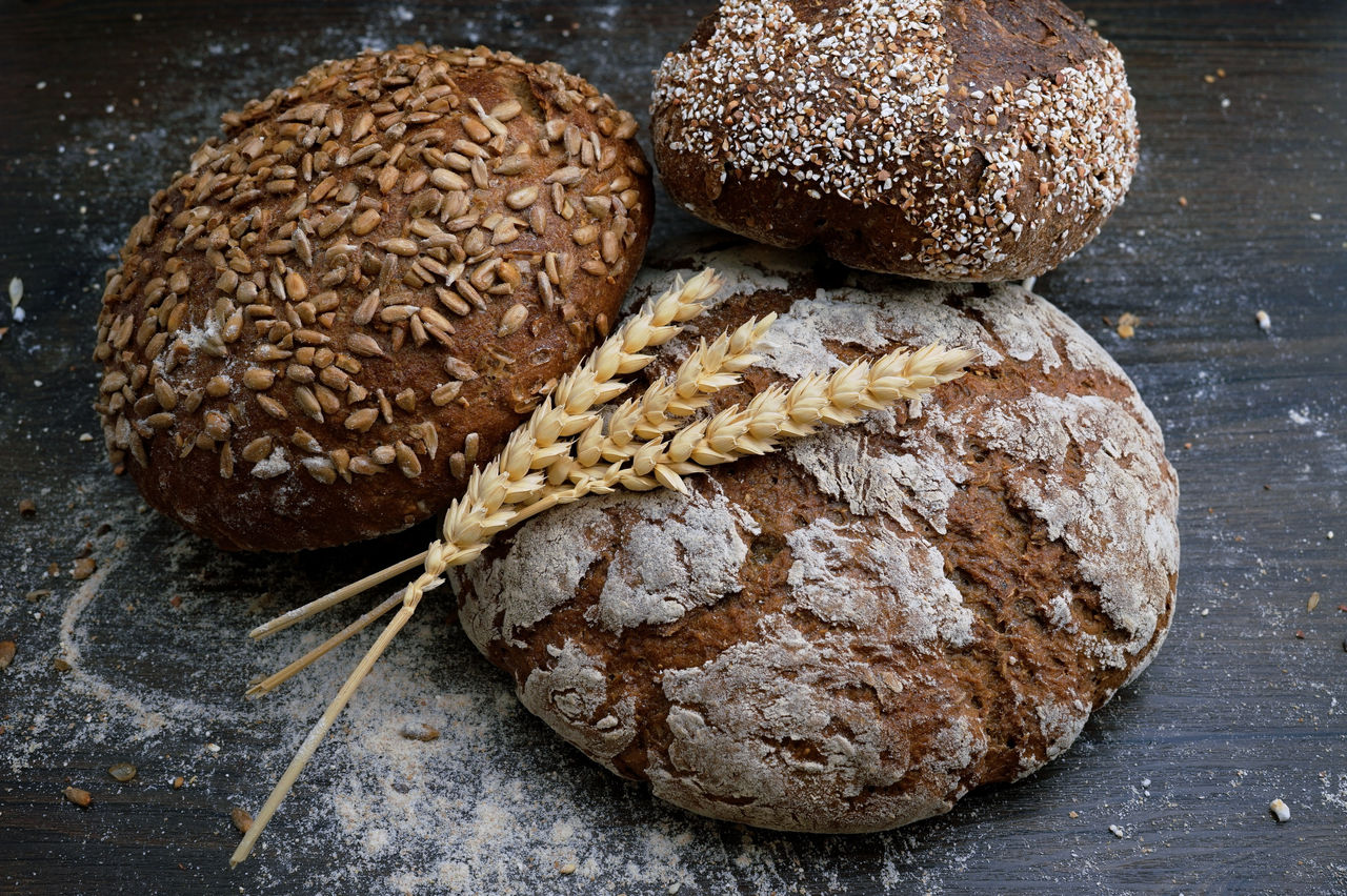 Three round bread loaves with seeds and pieces of wheat on top.